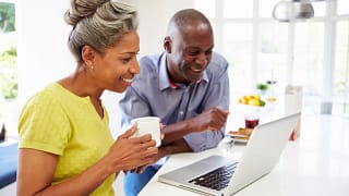 mature man and woman sitting in kitchen looking at laptop computer and smiling couple poc.jpg
