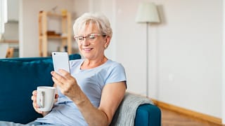 smiling senior holding coffee mug and looking at smartphone.jpg