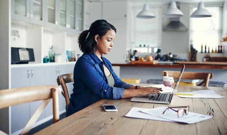 woman at kitchen table with laptop and paperw.width nlFF