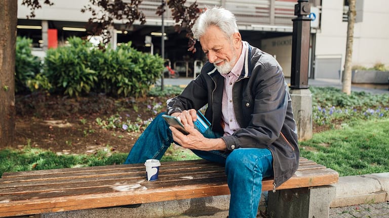 Older gentleman sitting on park bench using h.width Kwa
