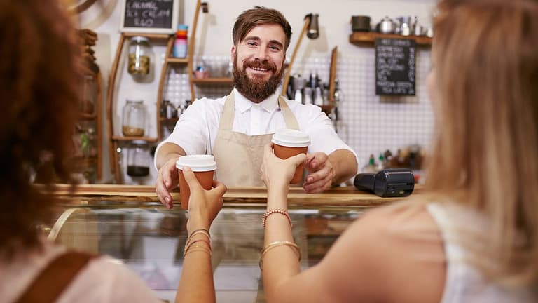 Smiling barista hands coffee to two women PAB.width .jpg