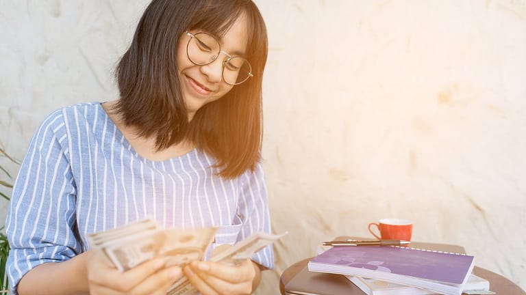 Young woman smiling as she counts cash in her.width XDyly.jpg