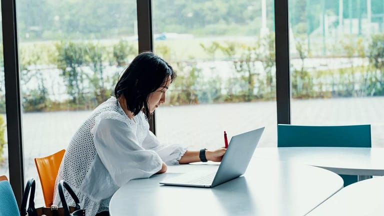 person writing at desk next to laptop DJgfk.width .jpg