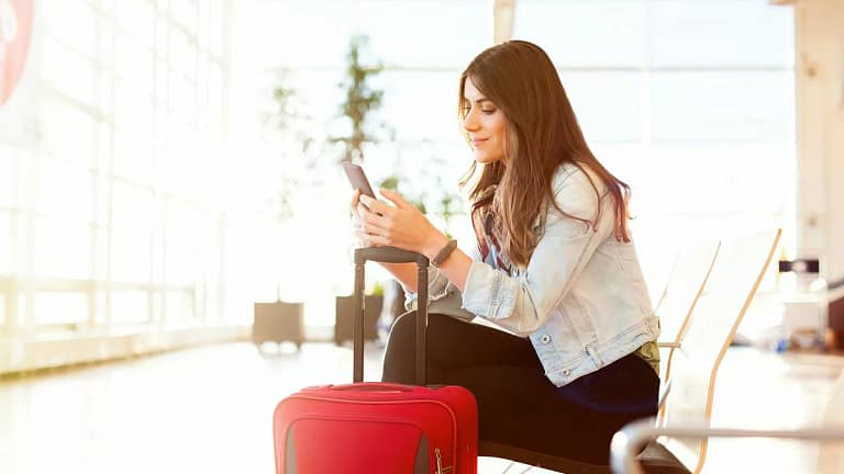 smiling woman with suitcase on phone in airpo.width KCyX.jpg