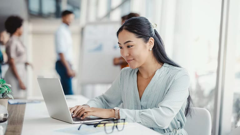 young person sitting at a desk in an office looking at a laptop.jpg