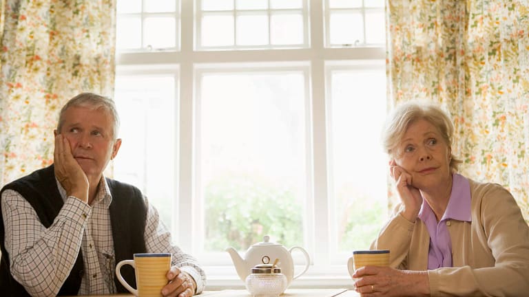 senior man and woman sitting at table resting their faces on their hands looking bored couple retirement.jpg
