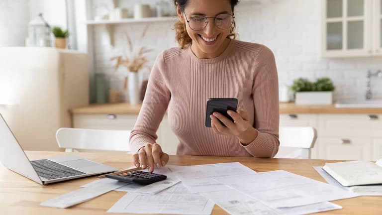 smiling person looking at smartphone and typing on calculator.jpg